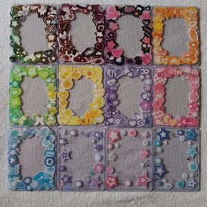 May include: A collection of twelve decorative photo frames. Each frame is rectangular with a clear center and a colorful border adorned with various shapes like hearts, stars, and flowers. The frames feature a variety of colors, including green, yellow, pink, and blue.