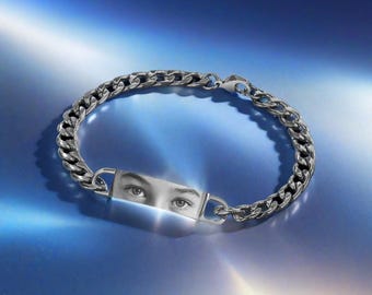 May include: Silver chain bracelet with a rectangular plate featuring a black and white image of a person's eyes. The bracelet has a lobster clasp closure and is displayed on a gradient blue background.