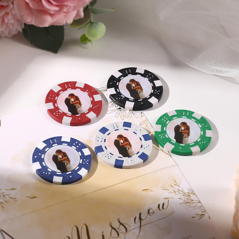 May include: Five poker chips in red, black, green, blue, and white, each featuring a photograph of a couple embracing. The chips are arranged on a white surface with floral and decorative elements.
