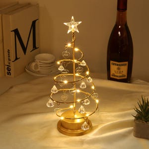May include: A gold-colored, spiral Christmas tree with a star on top and heart-shaped ornaments. The tree is illuminated with warm white lights and has crystal-like teardrop ornaments. A decorative item for the holiday season.