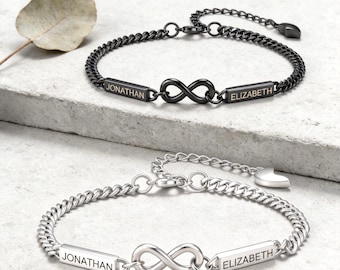 May include: Two curb chain bracelets featuring an infinity symbol centerpiece flanked by two rectangular bars engraved with the names JONATHAN and ELIZABETH. One bracelet is finished in matte black, and the other is finished in polished silver tone.