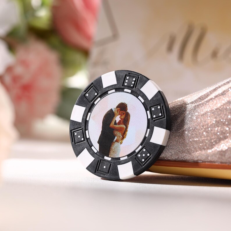 May include: A personalized poker chip with a black and white design. The chip features a photograph of a couple embracing. The chip has white squares and black triangles around the edge, with small white dots.