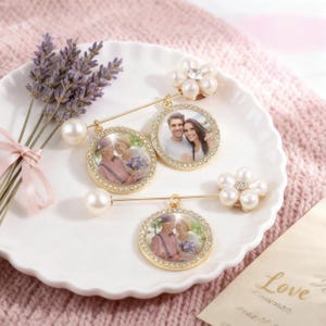 May include: Three gold photo brooches with crystal and pearl embellishments. Each brooch has a small photo in a circular frame. One brooch features a flower design with pearls and a central crystal.