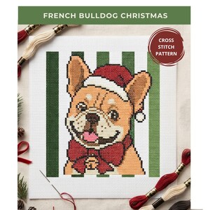 Op de afbeelding: Een kruissteekpatroon met een beige Franse bulldog die een rode kerstmuts en een rode vlinderdas met een belletje draagt. De hond is gecentreerd tegen een achtergrond van verticale groene en witte strepen. De tekst luidt FRENCH BULLDOG CHRISTMAS.