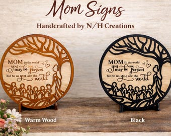 May include: Two 8-inch round wooden signs with the text "Mom" and a family tree design. One sign is warm wood, the other is black. The signs are handcrafted and include the text "Custom Colors for Every Style."