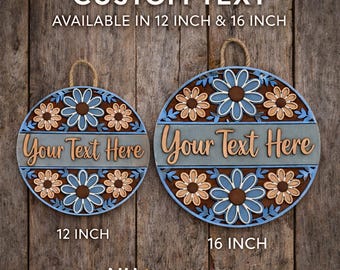 May include: Two round wooden signs with a floral design and the text "Your Text Here". The signs are available in 12-inch and 16-inch sizes. The signs have a blue, brown, and tan color scheme and a rope hanger.