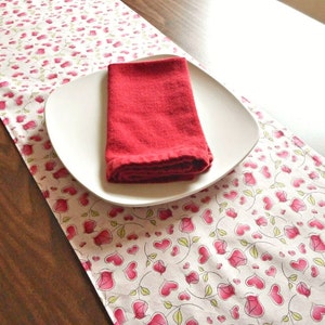 May include: A white table runner with a pink heart pattern and a red napkin on a white plate.