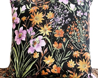 Pode incluir: Uma almofada preta com um padrão floral com flores rosa, laranja e amarelas sobre um fundo preto.