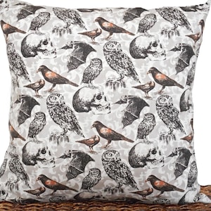 May include: A white throw pillow with a repeating pattern of black bats, owls, skulls, and birds. The pattern is on a light gray background.