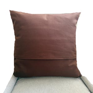 Pode incluir: Uma capa de almofada quadrada em cor castanho escuro s&oacute;lido. A almofada apresenta uma costura horizontal na parte inferior, indicando um design de fecho tipo envelope. O tecido parece liso e mate, proporcionando uma apar&ecirc;ncia simples e uniforme.