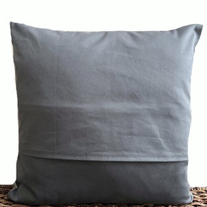 May include: A square throw pillow cover in a solid dark gray color. The cover features a horizontal envelope-style closure flap across the lower section, secured with visible stitching along the edge of the fabric fold, creating a clean finish.