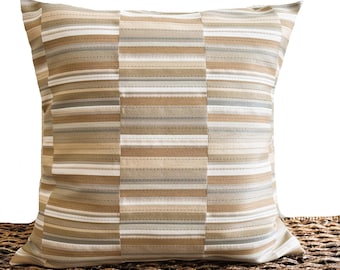 Pode incluir: Almofada decorativa quadrada com um padrão listrado em tons de bege, castanho e branco. A almofada tem um design costurado e é colocada sobre uma superfície tecida. Um artigo de decoração para casa.