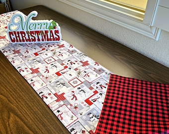 May include: A white table runner with a snowman pattern and red trim. The runner is on a wooden table and has a sign that says "Merry Christmas" on top of it.
