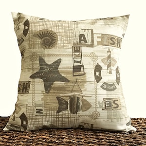 May include: A beige and brown throw pillow with a nautical theme. The pillow features a starfish, fish, anchor, and various text including "Welcome Aboard" and "I Like Fish".