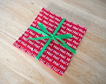 May include: A stack of red fabric squares with a white "Ho! Ho!" pattern, tied together with a green ribbon.
