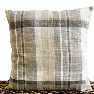 May include: A square throw pillow featuring a woven plaid pattern in neutral shades of beige, light gray, dark charcoal, and soft white. The fabric has a visible textured weave, and the design consists of intersecting vertical and horizontal stripes.