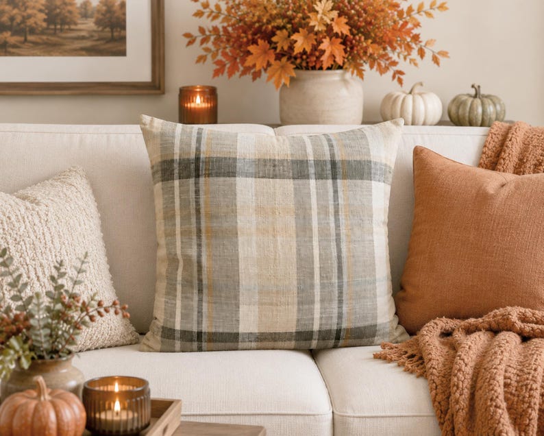 May include: A square throw pillow featuring a woven plaid pattern in neutral shades of beige, cream, gray, and muted brown. The fabric has a visible linen-like texture with intersecting vertical and horizontal lines forming a classic grid design.