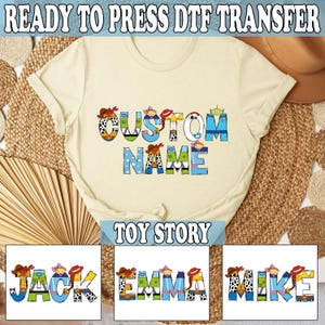 May include: Cream-colored t-shirt with the words "CUSTOM NAME" in colorful, cartoon-style letters. The shirt features a "Toy Story" theme, with additional text at the top and bottom. Below are three examples of names: JACK, EMMA, and MIKE.