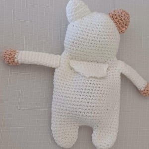 May include: White crocheted stuffed animal with pink ears and arms. The toy is in the shape of a bear.