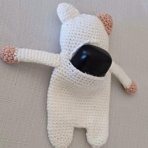 May include: White crocheted stuffed animal with pink ears and a black remote control inside. The stuffed animal is shaped like a bear.