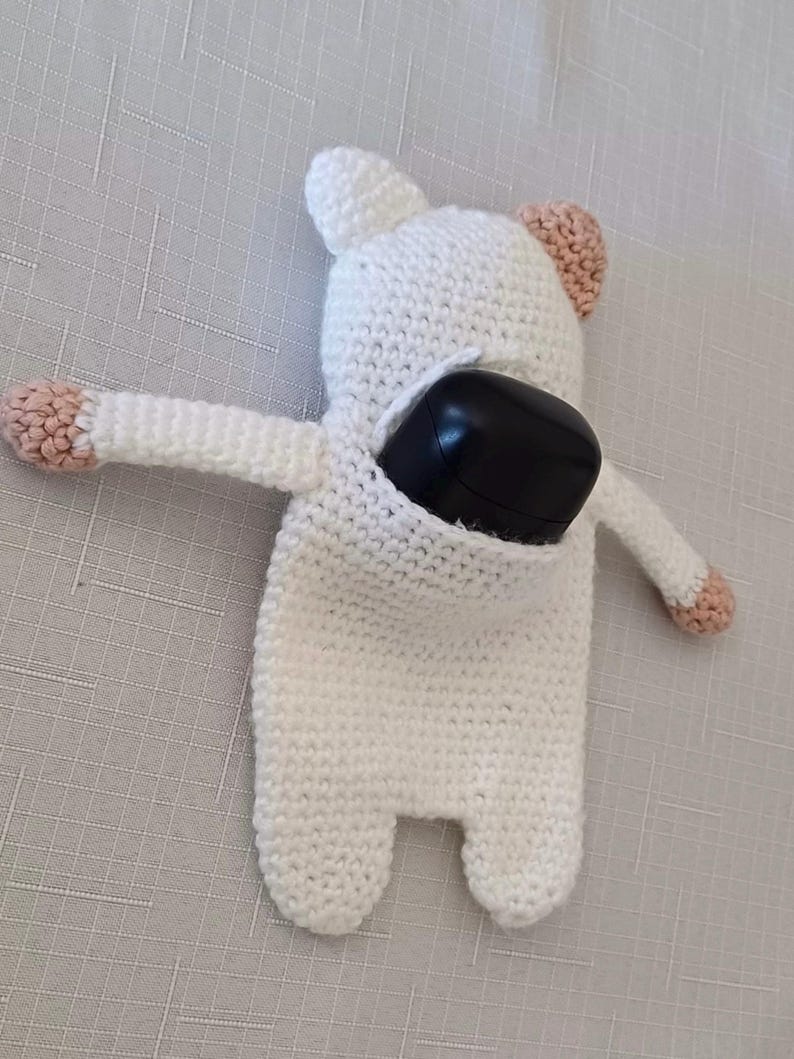 May include: White crocheted stuffed animal with pink ears and a black remote control inside. The stuffed animal is shaped like a bear.