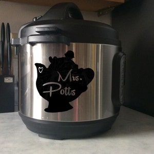 Könnte beinhalten: Ein elektrischer Schnellkochtopf aus Edelstahl mit einer schwarzen Silhouette von Mrs. Potts aus Disneys Die Schöne und das Biest. Die Silhouette enthält ein Herz und den Text "Mrs. Potts".