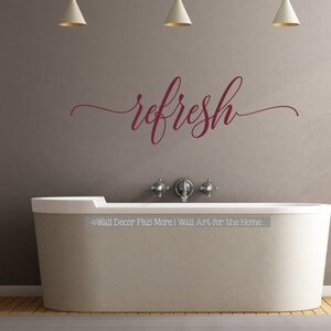 May include: A white bathtub with a burgundy vinyl decal that reads "refresh" on a grey wall with three white pendant lights.