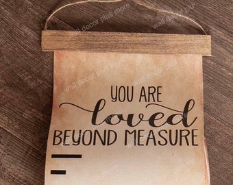 May include: A rustic brown wooden scroll with a white background and black text that reads "You are loved beyond measure". The scroll is hanging from a brown twine rope and is attached to a wooden dowel.