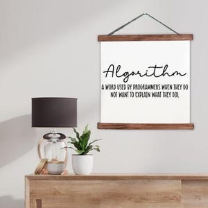 May include: A white wall hanging with dark brown wooden rails at the top and bottom, featuring the black text: Algorithm, A word used by programmers when they do not want to explain what they did. The sign is suspended by a thin dark string.