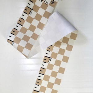 May include: A brown and white checkered growth chart with black numbers and a black wooden top. The chart is rolled up and has the names "Evelyn Beth" written on it.