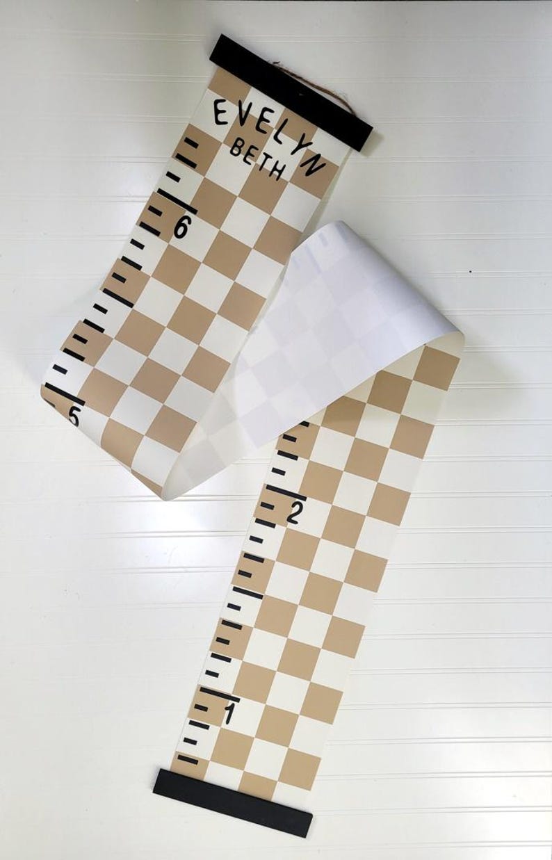 May include: A brown and white checkered growth chart with black numbers and a black wooden top. The chart is rolled up and has the names "Evelyn Beth" written on it.