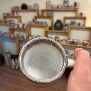 May include: A gray and orange speckled ceramic mug with a white interior and a handle. The mug is empty.