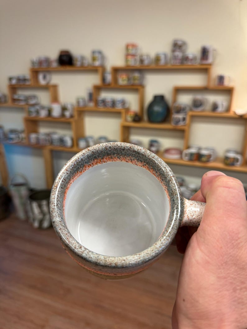 May include: A gray and orange speckled ceramic mug with a white interior and a handle. The mug is empty.