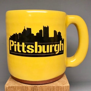 May include: Yellow ceramic mug with a black silhouette of the Pittsburgh skyline and the word "Pittsburgh" printed on the front.