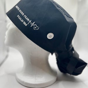 May include: Black scrub hat with a white embroidered design that reads "Faith Over Fear - Psalm 118:6" with a heart and a heartbeat graphic. The hat has a button on the top.