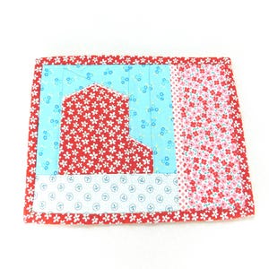 May include: A red, white, and blue patchwork coaster with a floral pattern. The coaster is made of fabric and has a quilted design.