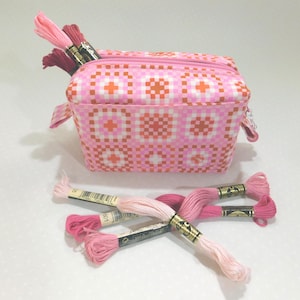 May include: A pink and orange zippered pouch with a geometric pattern. The pouch is filled with pink embroidery floss.