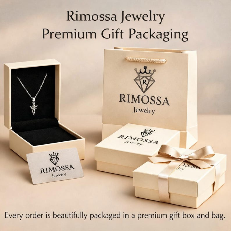 May include: A silver necklace with a pendant in an open jewelry box, a gift bag, and two gift boxes with ribbons. The boxes and bag are beige with the "Rimossa Jewelry" logo. The text reads "Premium Gift Packaging".