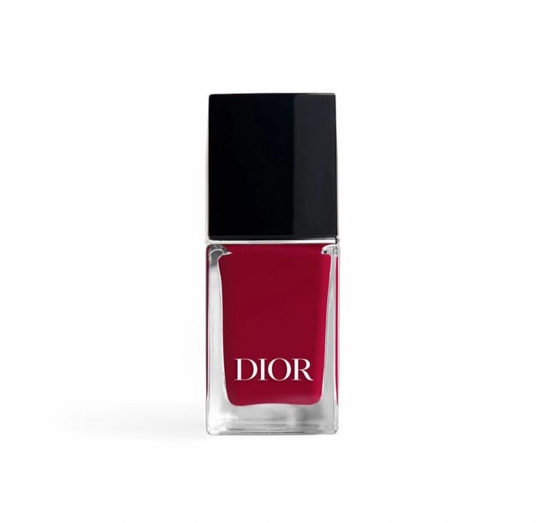 May include: A bottle of red nail polish with a black cap. The clear glass bottle has a rectangular shape and the word "DIOR" is printed in white on the front.