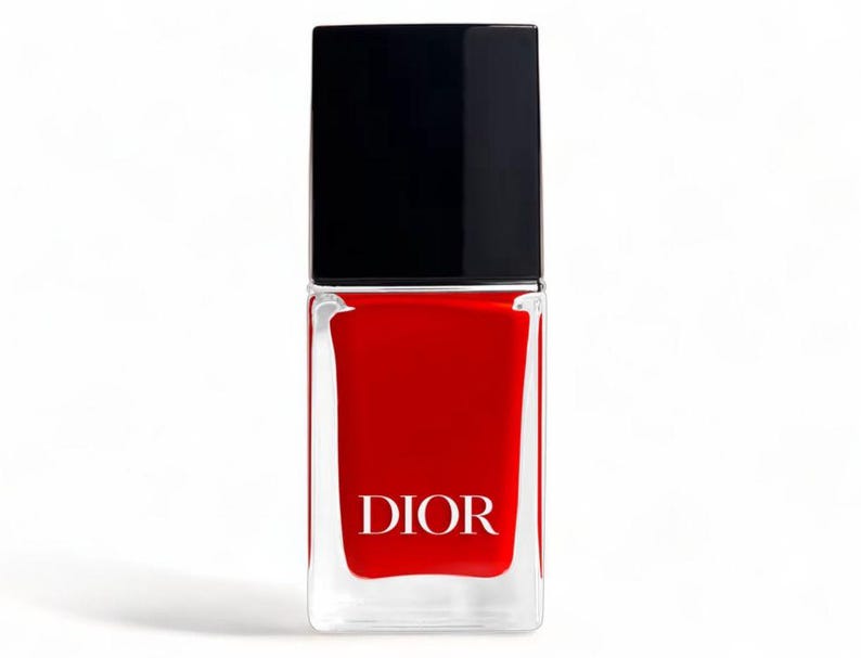 May include: A bottle of red nail polish with a black cap. The clear glass bottle has the word "DIOR" printed in white. The nail polish is a vibrant, solid red color.