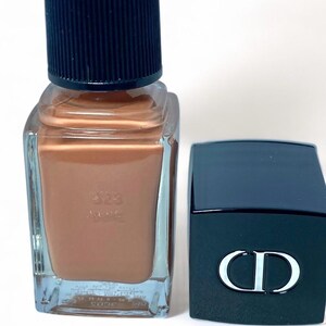 Peut inclure: Un flacon de vernis &agrave; ongles avec un liquide de couleur bronze et un bouchon noir. &Agrave; c&ocirc;t&eacute;, une bo&icirc;te noire rectangulaire avec un logo "CD" blanc. Le flacon de vernis &agrave; ongles porte le num&eacute;ro "303".