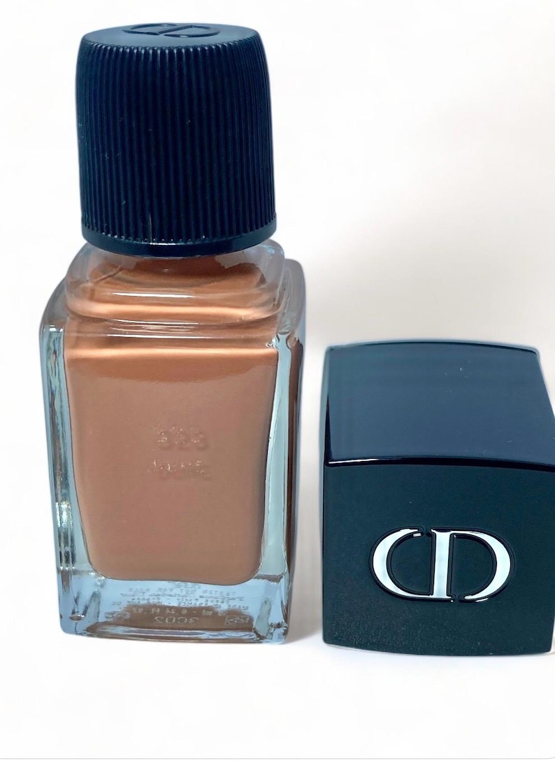 Peut inclure: Un flacon de vernis &agrave; ongles avec un liquide de couleur bronze et un bouchon noir. &Agrave; c&ocirc;t&eacute;, une bo&icirc;te noire rectangulaire avec un logo "CD" blanc. Le flacon de vernis &agrave; ongles porte le num&eacute;ro "303".