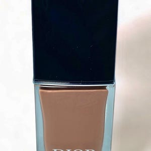 Peut inclure: Un flacon de vernis &agrave; ongles Dior. Le flacon est rectangulaire avec un bouchon noir et un corps en verre transparent. La couleur du vernis &agrave; ongles est un marron chaud. Le mot "DIOR" est imprim&eacute; en blanc sur le devant du flacon.