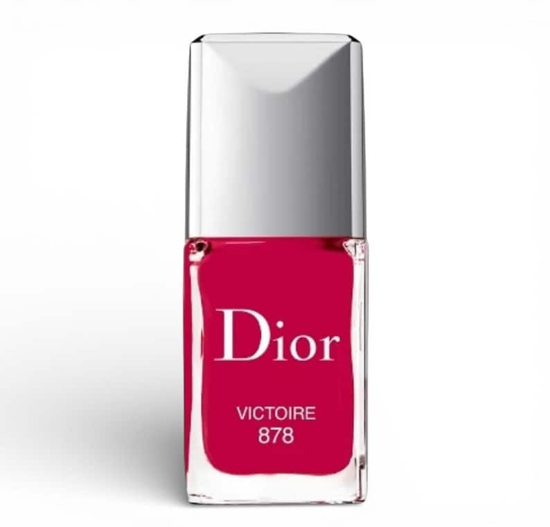 May include: A bottle of Dior nail polish in a vibrant shade of red. The bottle has a rectangular shape with a silver cap. The word "Dior" is prominently displayed on the front, along with "VICTOIRE 878".