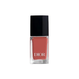 May include: A bottle of Dior nail polish. The square glass bottle contains a coral-colored polish and is topped with a black square cap. The word "DIOR" is printed in white on the front of the bottle.