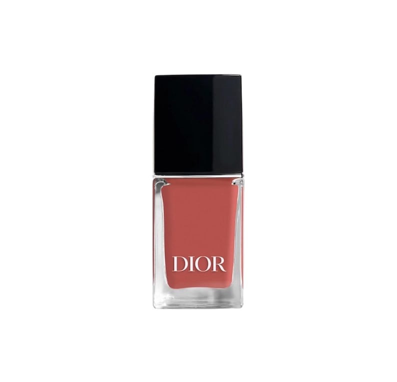 May include: A bottle of Dior nail polish. The square glass bottle contains a coral-colored polish and is topped with a black square cap. The word "DIOR" is printed in white on the front of the bottle.