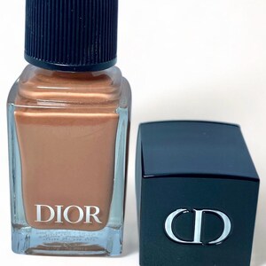 Peut inclure: Un flacon de vernis &agrave; ongles Dior avec un vernis de couleur bronze &agrave; l'int&eacute;rieur. Le flacon a un corps en verre transparent et un bouchon bleu fonc&eacute;. Le logo Dior est imprim&eacute; en blanc sur le devant. Un bouchon bleu fonc&eacute; s&eacute;par&eacute; avec le logo CD est &agrave; c&ocirc;t&eacute; du flacon.
