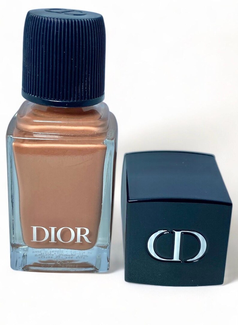 Peut inclure: Un flacon de vernis &agrave; ongles Dior avec un vernis de couleur bronze &agrave; l'int&eacute;rieur. Le flacon a un corps en verre transparent et un bouchon bleu fonc&eacute;. Le logo Dior est imprim&eacute; en blanc sur le devant. Un bouchon bleu fonc&eacute; s&eacute;par&eacute; avec le logo CD est &agrave; c&ocirc;t&eacute; du flacon.
