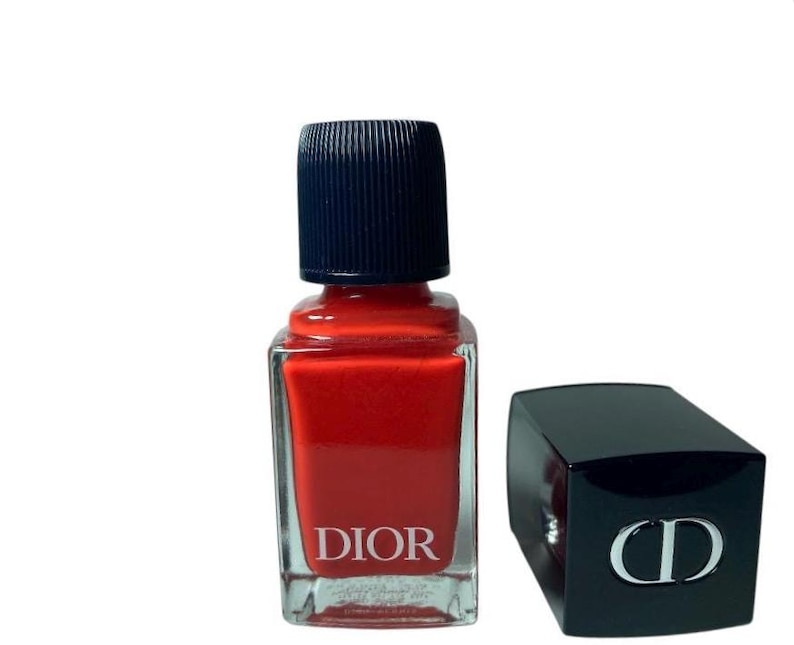 May include: A bottle of Dior nail polish in a vibrant red hue, with a black cap and the brand name printed on the front. The cap is off to the side, revealing the iconic CD logo.