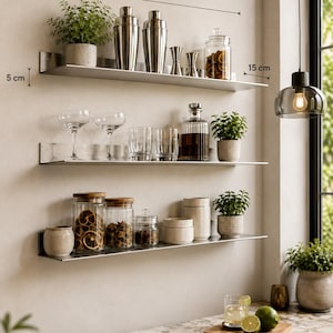 Puede incluir: Tres estantes horizontales de acero inoxidable, cada uno de 73 cm de largo, 15 cm de profundidad y 5 cm de alto. Los estantes contienen frascos de vidrio, cocteleras de metal, vasos y plantas pequeñas. El texto inferior dice: Premium Stainless Steel, Strong & Durable High Load Capacity, Sleek Satin Finish Easy to Clean.